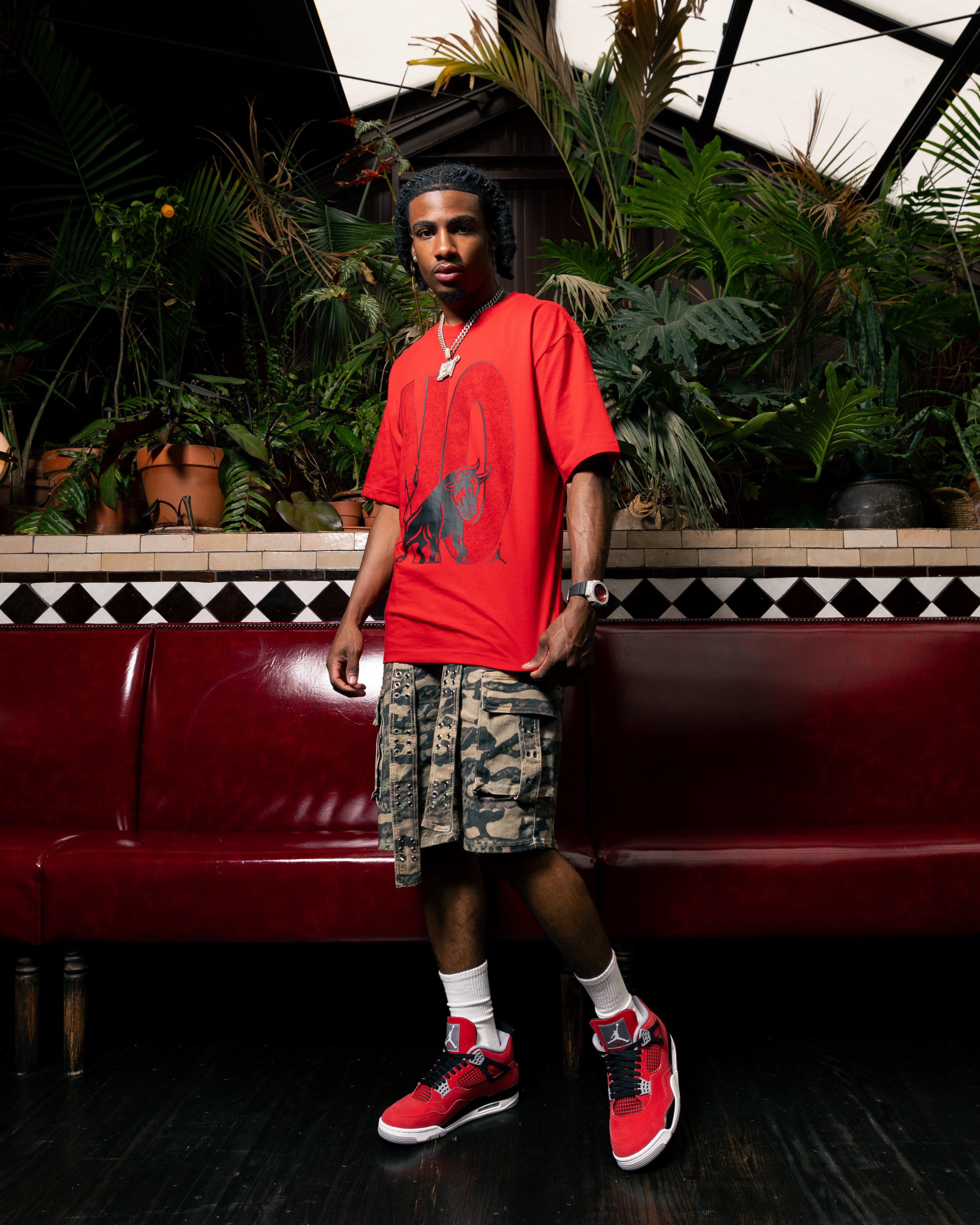 Person in red graphic T-shirt and camo shorts standing by red booth, wearing red sneakers.