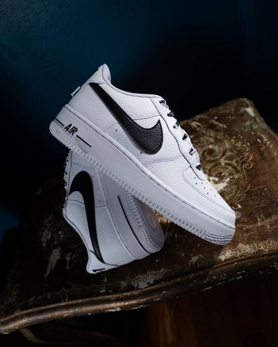 White Nike Air Force 1 sneakers with black Swooshes displayed on a vintage wooden table.
