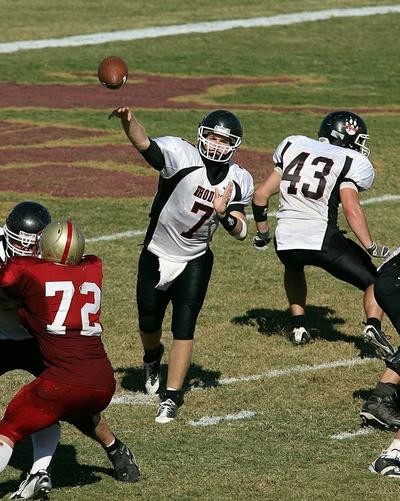 Football quarterback in a white-and-black uniform throwing a pass as players block nearby opponents on the field.