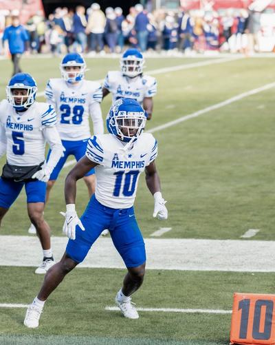 Memphis football players in white-and-blue uniforms warming up together near the sideline.