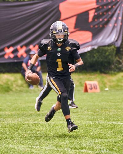 Football player in a black-and-gold uniform running with the ball during a game.