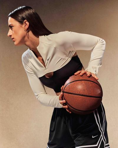 Person holding a basketball while wearing a white Nike quarter-zip top over a black athletic top and black Nike basketball shorts.