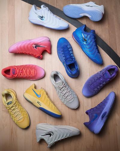 Overhead view of Nike basketball shoes in white, blue, pink, yellow, gray and purple arranged on a hardwood basketball court.