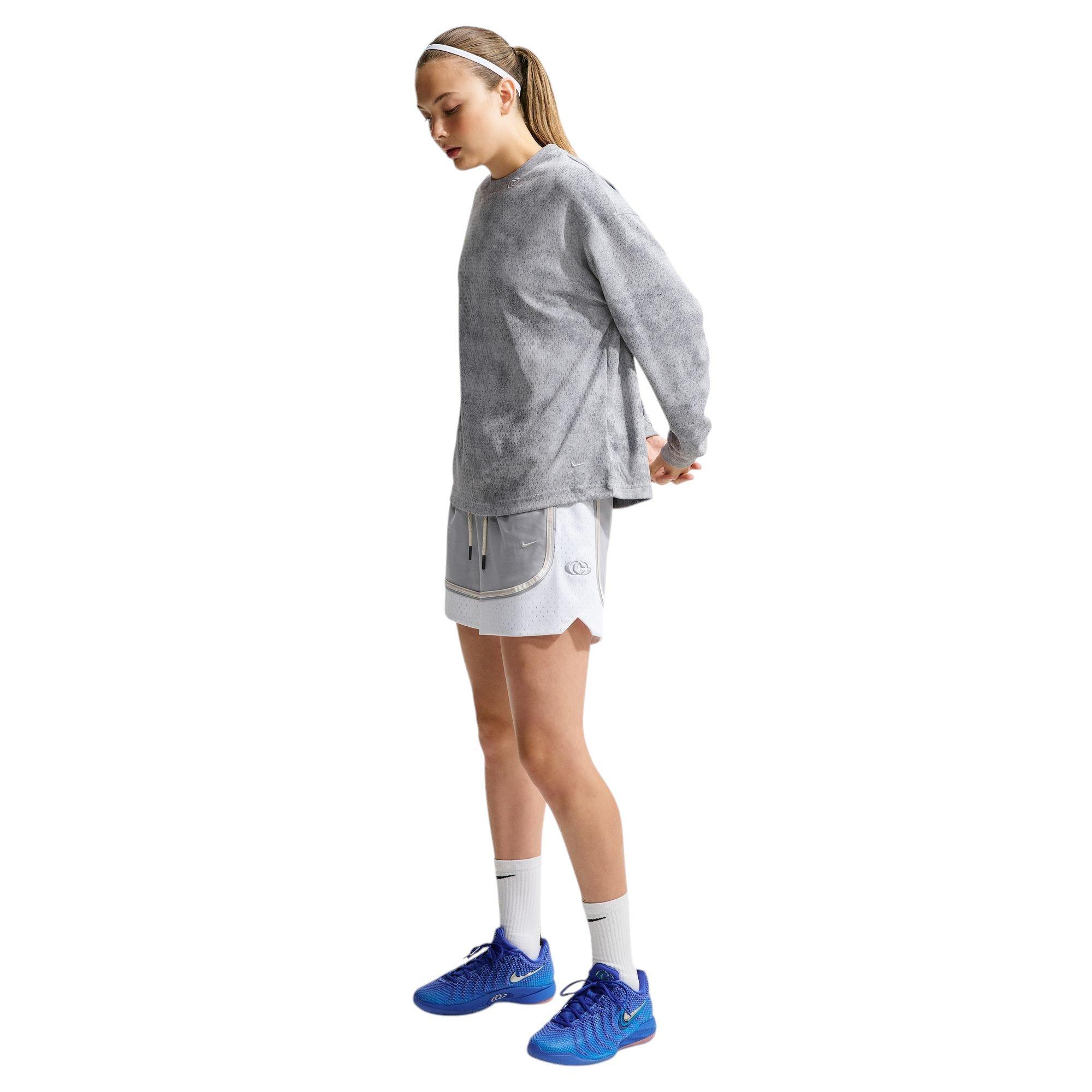 Model wearing an oversized gray Nike long-sleeve top, gray-and-white basketball shorts and blue Nike basketball shoes.