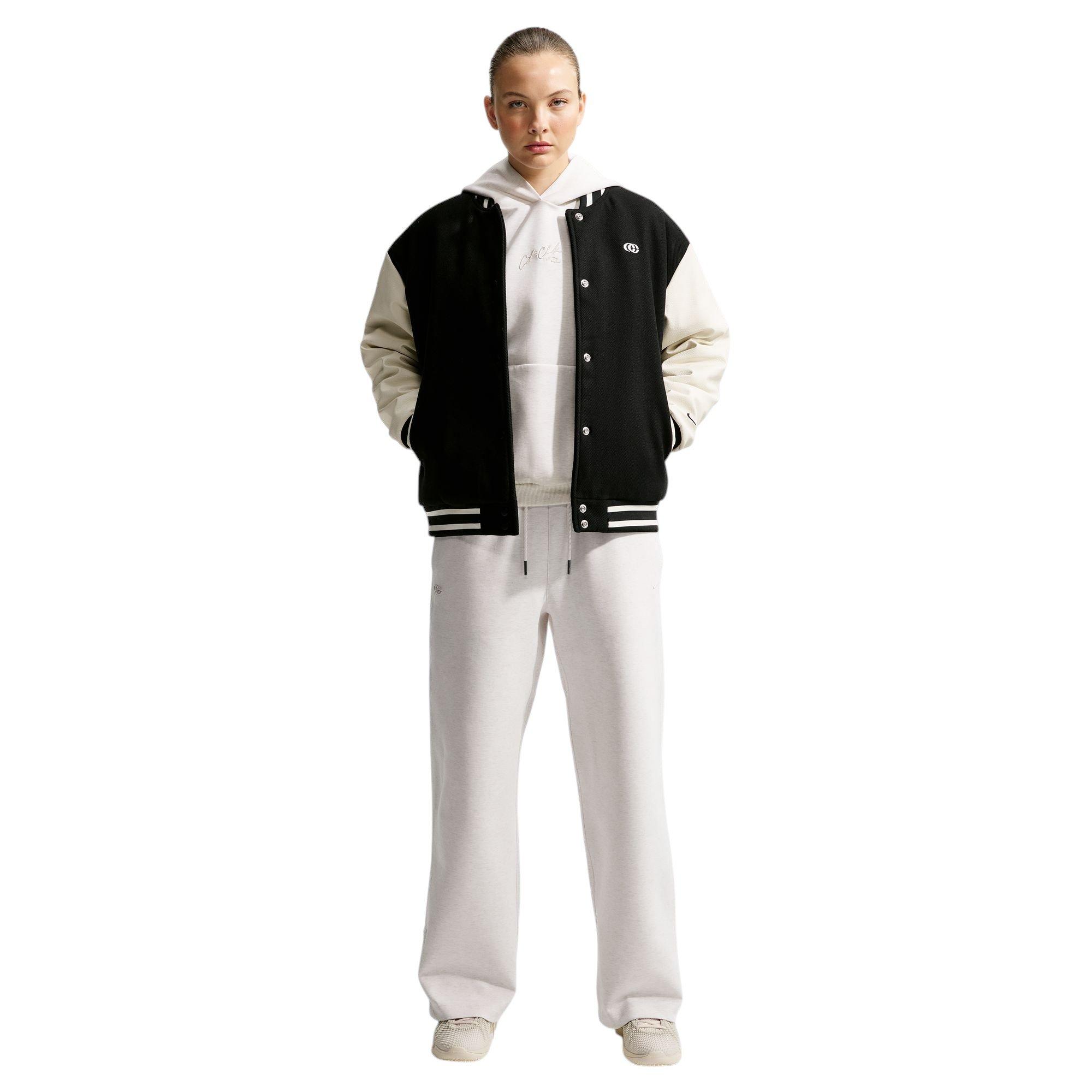 Model wearing a black-and-cream varsity jacket over a cream hoodie with matching wide-leg sweatpants and neutral sneakers.