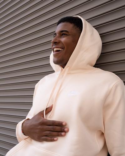 Person wearing a light peach Nike hoodie with the hood up, shown in close-up against a gray metal roll-up door.