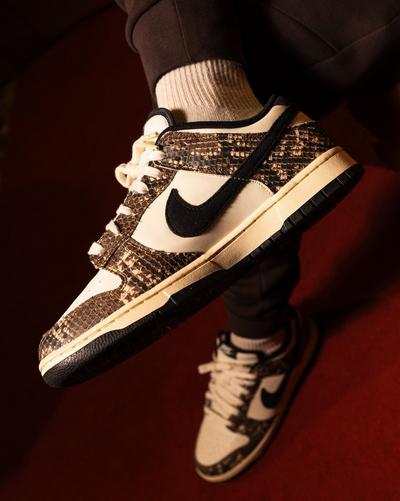 Close-up of a Nike Dunk Low sneaker featuring cream leather, brown snakeskin overlays, a black suede Swoosh and white laces.