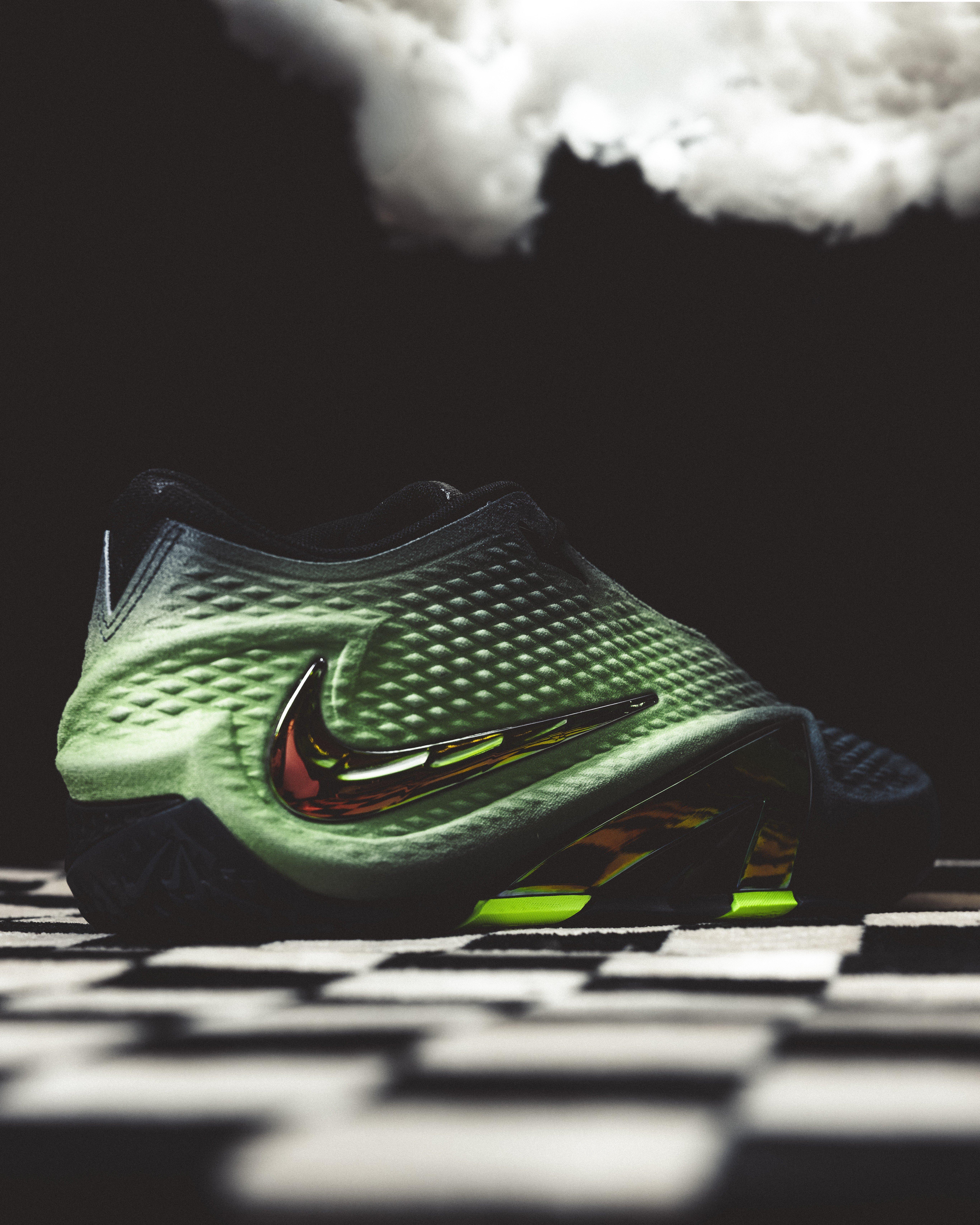 Close-up of the Nike Ja 4 Nightmare heel showing a green textured upper, black collar, iridescent Nike Swoosh and dark midsole against a smoky black background.