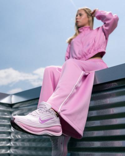 Person wearing a pink tracksuit and pink Nike Vomero Plus running shoes while seated on outdoor metal steps.