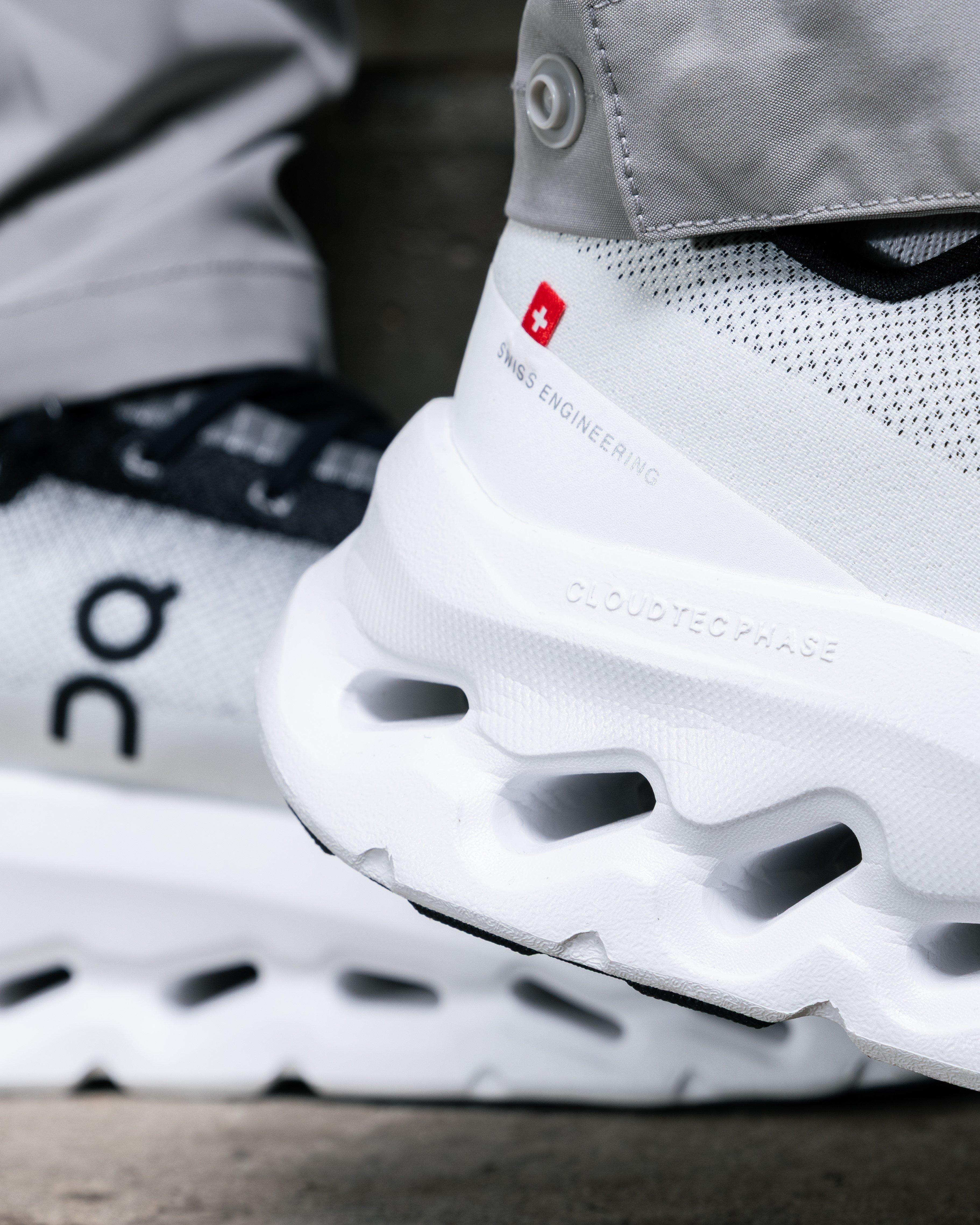 A detailed, close-up shot of the heel of a white On sneaker. The Swiss flag, "Swiss Engineering," and "Cloudtec Phase" are visible on the side of the shoe, and the shoe's thick, perforated sole is prominent.