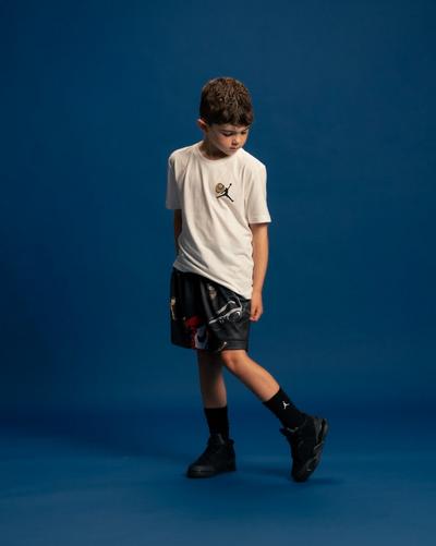 Child wearing a white Jordan T-shirt, graphic shorts and black sneakers against a blue background