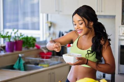 Nourish Your Body - woman eating bowl of fruit in kitchen