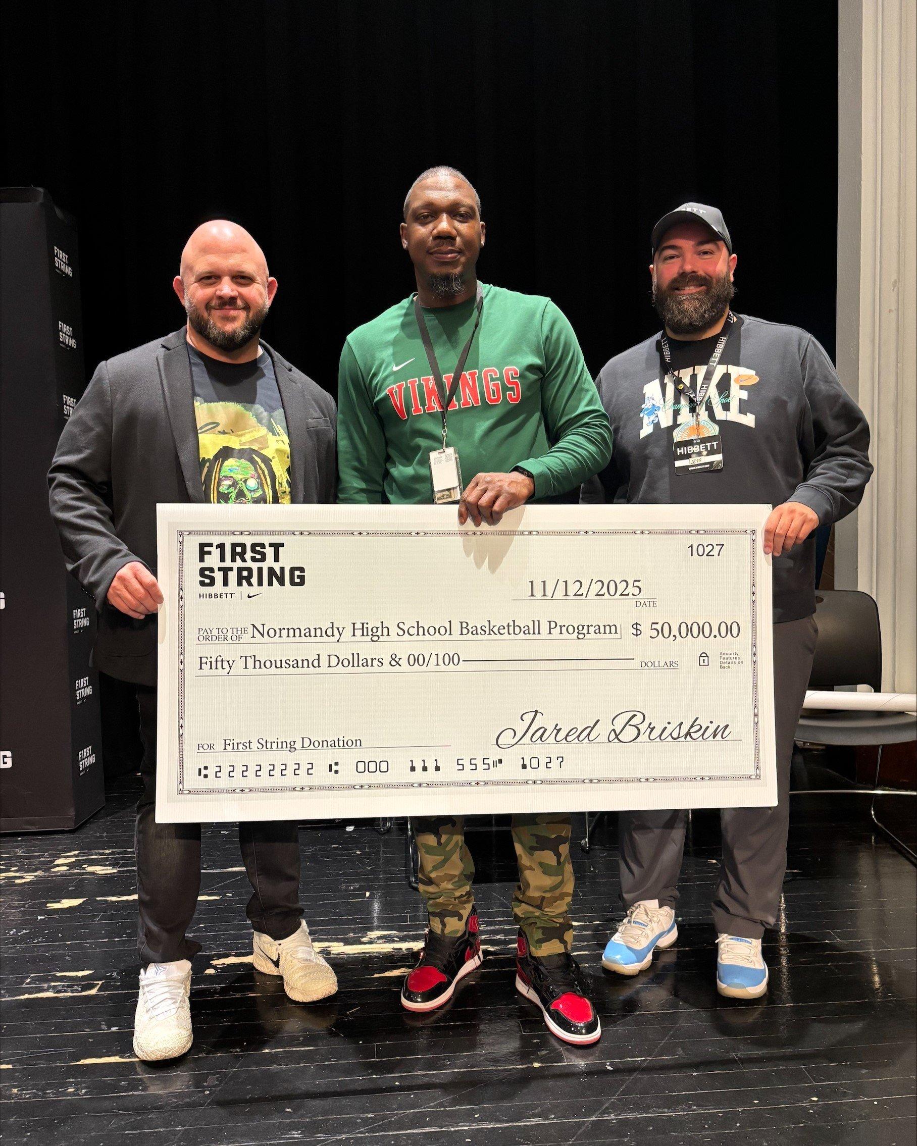 Three men, including a Normandy High School coach in a Vikings shirt and a Hibbett representative, holding the $50,000 donation check for the school's basketball program