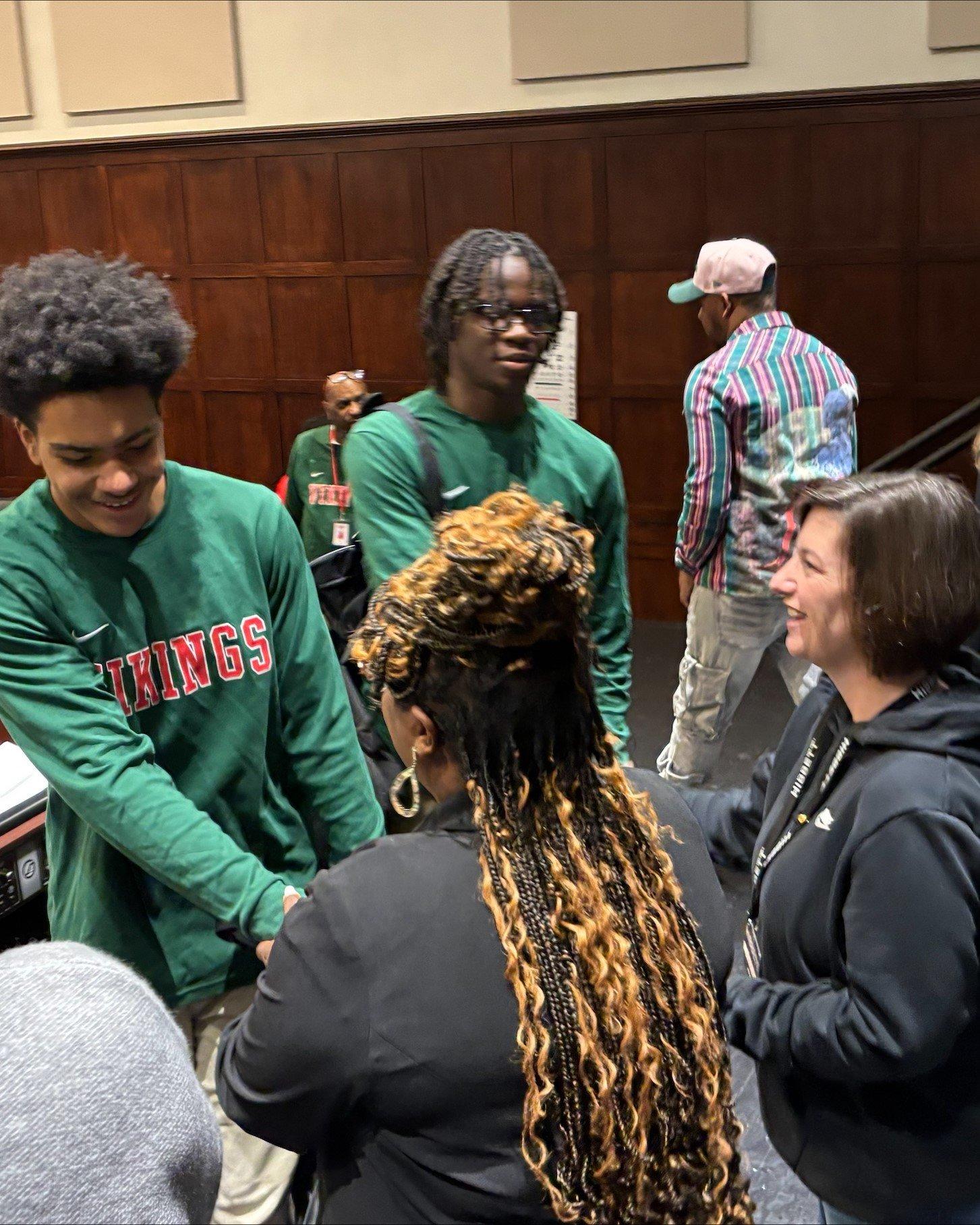 A Normandy High School basketball player shaking hands with event organizers while a Hibbett team member smiles nearby.
