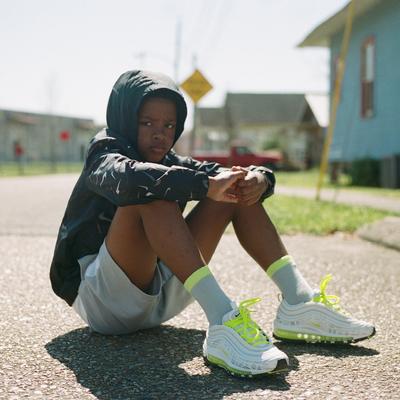 Reggie Ward's son seated on asphalt in Nike AM 97s