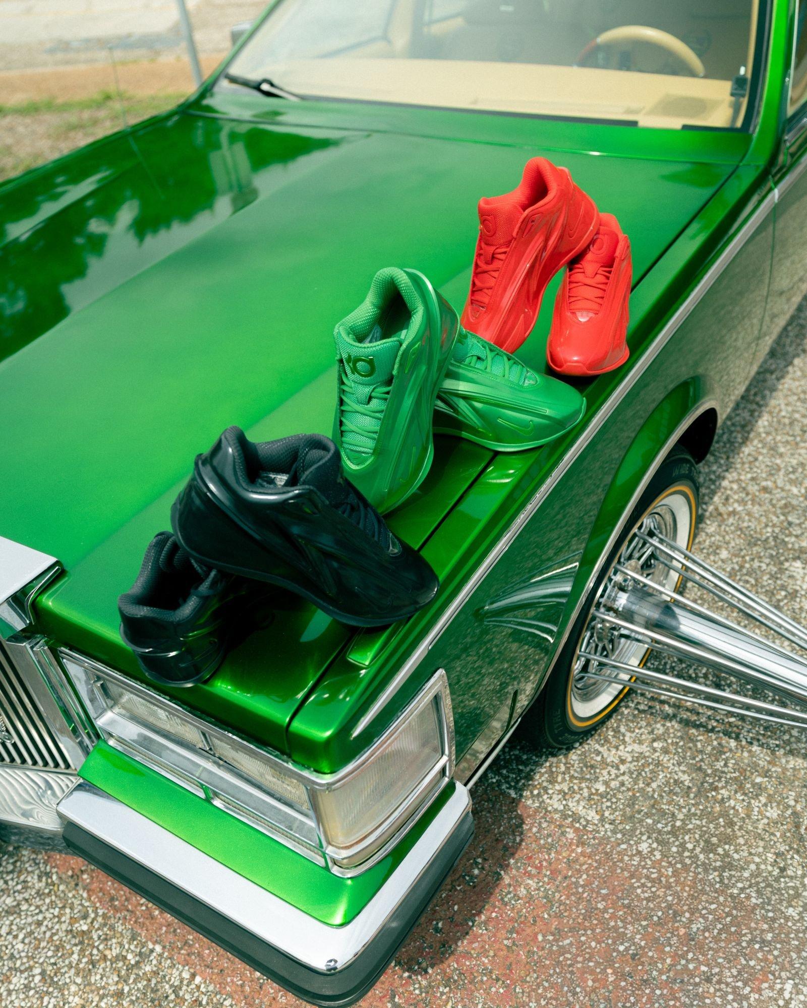 Nike KD 19 basketball shoes in black, green, and red colorways displayed on the hood of a custom green classic car with chrome wire-spoke wheels.