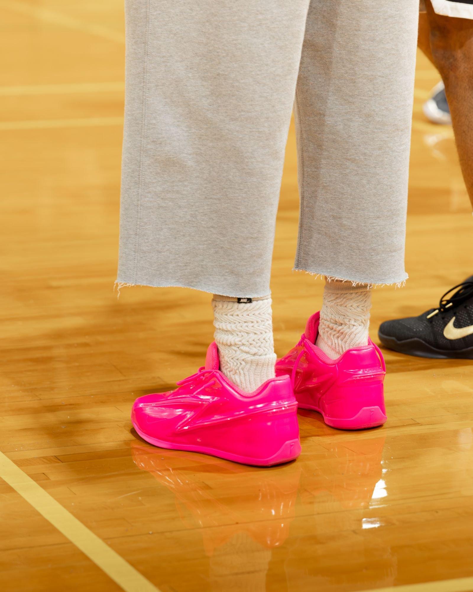 Bright pink Nike KD 19 basketball shoes paired with cream knit socks on an indoor basketball court, highlighting the vibrant sneaker colorway during a community basketball event.