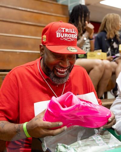 Bright pink Nike KD 19 basketball shoe being presented during a community event, with the sneaker held above an open shoebox in an indoor gymnasium setting.