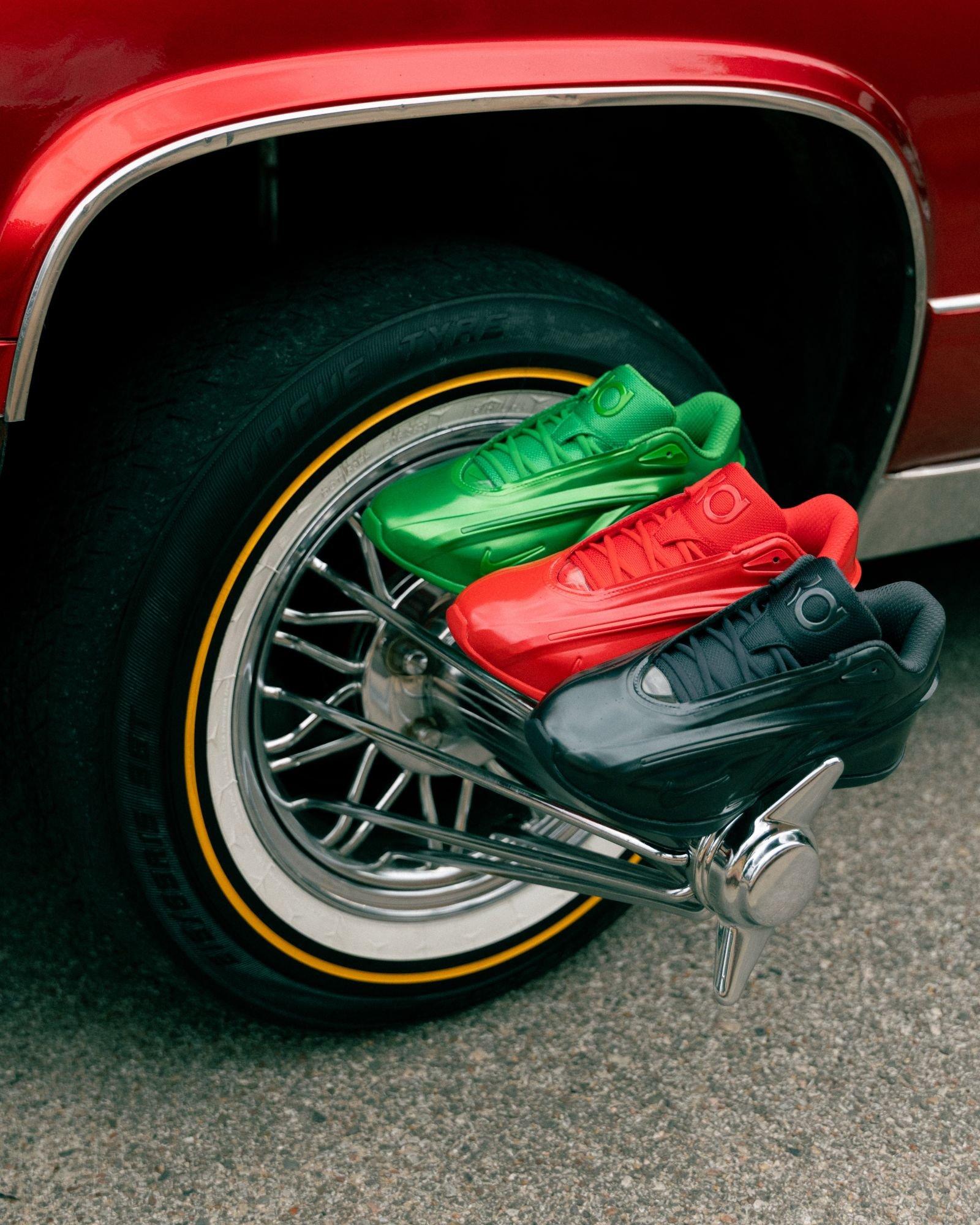 Nike KD 19 basketball shoes in green, red, and black colorways displayed on a classic car wire-spoke wheel, highlighting the sneaker collection in an outdoor setting.