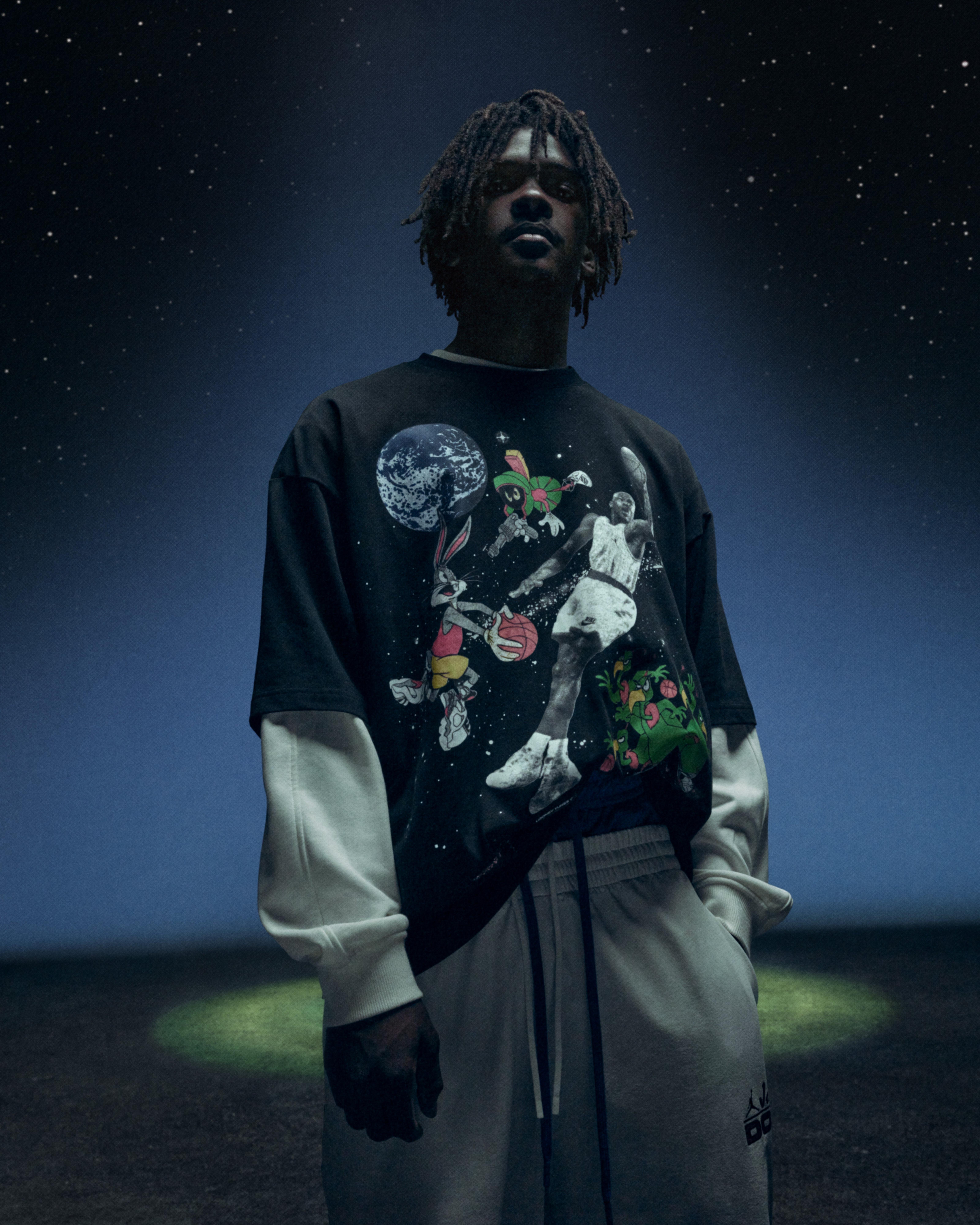 Person wearing a black Space Jam graphic T-shirt featuring Michael Jordan, Bugs Bunny, Marvin the Martian and other Looney Tunes characters, layered over a white sweatshirt.