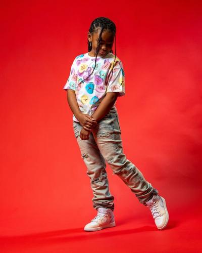 Gemini said A young girl wearing a white t-shirt with colorful heart graphics, distressed light-wash jeans, and high-top sneakers poses against a solid red background.