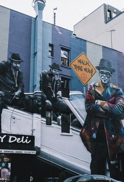 An outdoor shot of a stack of five pairs of Saucony sneakers in various colors, including white, pink, black, and blue. The shoes are resting on a concrete ledge with graffiti on a blue and white background.