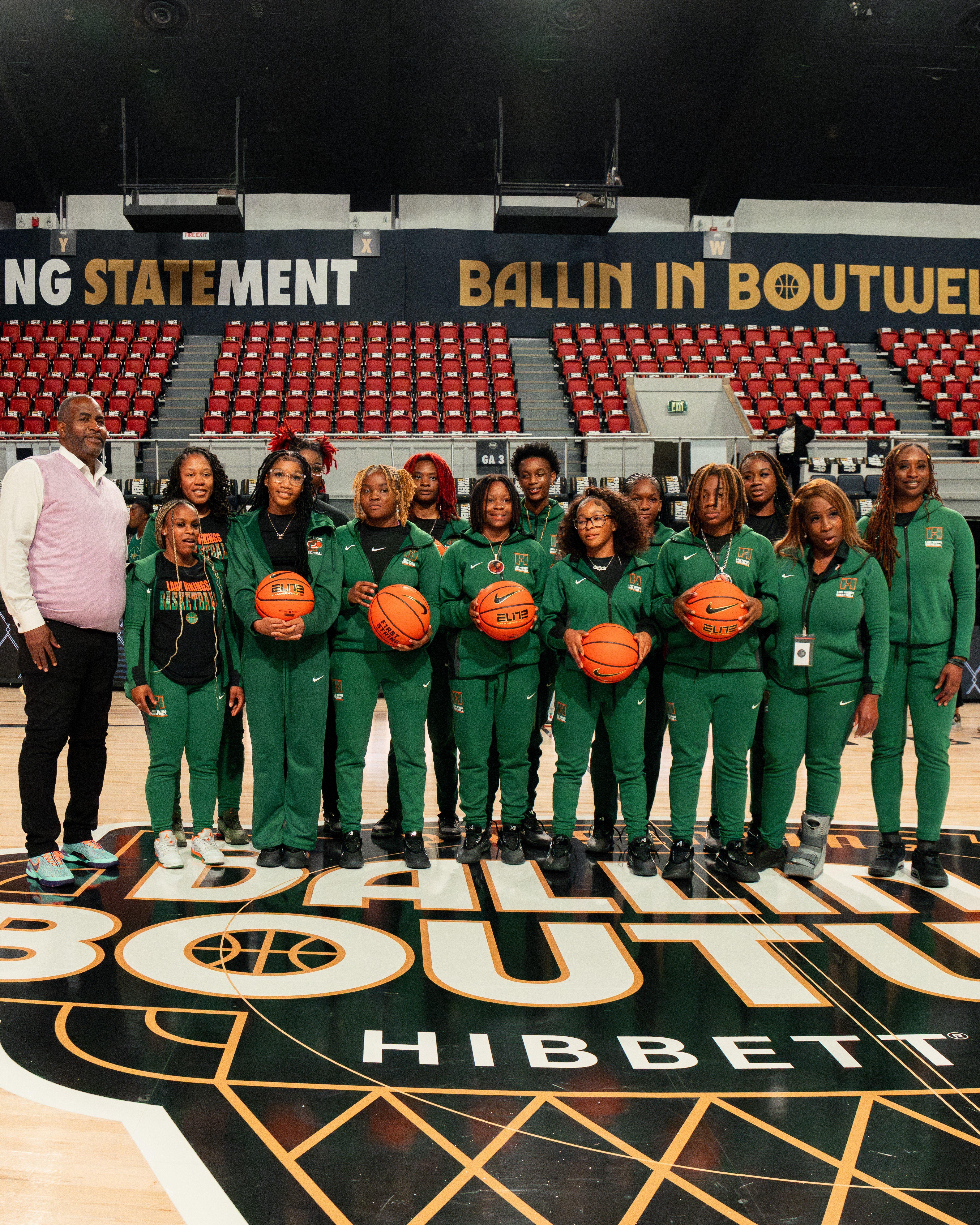 A group photo of the Huffman High School Girls Basketball team and their coaches, standing on the court in matching green tracksuits while holding basketballs