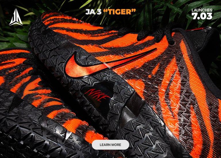 Promotional image featuring the JA 3 TIGER basketball shoes. The sneakers display an orange and black tiger-stripe pattern set against a background of green ferns. The graphic also includes a LEARN MORE button and notes a launch date of 7.03.