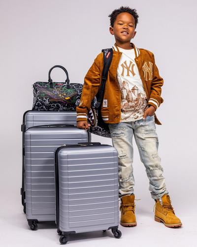 Child wearing a brown Yankees jacket and Timberland boots beside silver luggage.