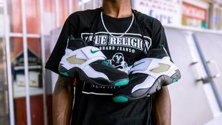 A studio shot of the Nike Air Diamond Turf '93 "Emerald" men's shoe on a white background. The sneakers are black and white with emerald green accents, and a prominent white midfoot strap. The shoe features a durable leather upper, with Nike Air cushioning in the heel and forefoot. It is a cross-trainer silhouette from Deion Sanders' signature line. The shoe will be released on August 29, 2025
