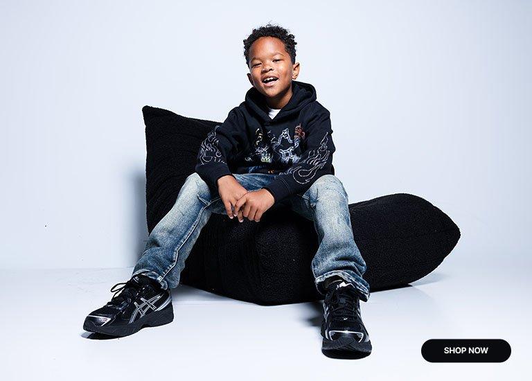 Kid wearing a graphic hoodie, jeans and black ASICS sneakers.