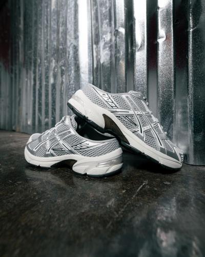Silver and white ASICS running shoes with metallic accents on a dark floor against an industrial metal backdrop.Provide your feedback on BizChat