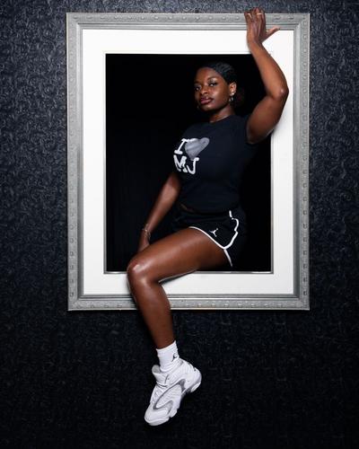 Person wearing a black graphic tee, athletic shorts, and white sneakers posed within a decorative picture frame.