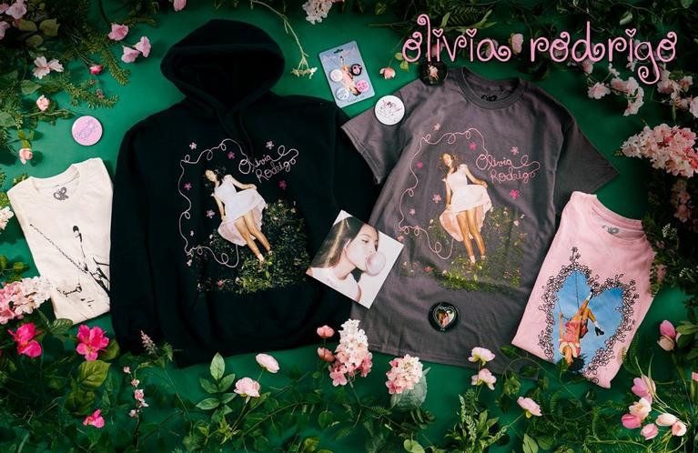 Olivia Rodrigo graphic hoodie and T-shirts with pins, laid out with flowers. Shop Now.