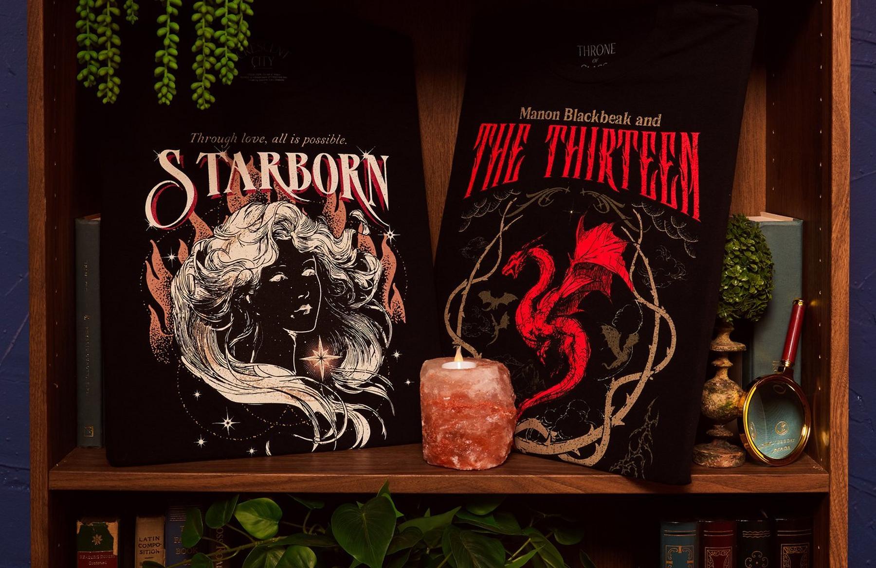 Two bookish graphic T-shirts, “Starborn” and “The Thirteen,” displayed on a shelf. Shop Now.