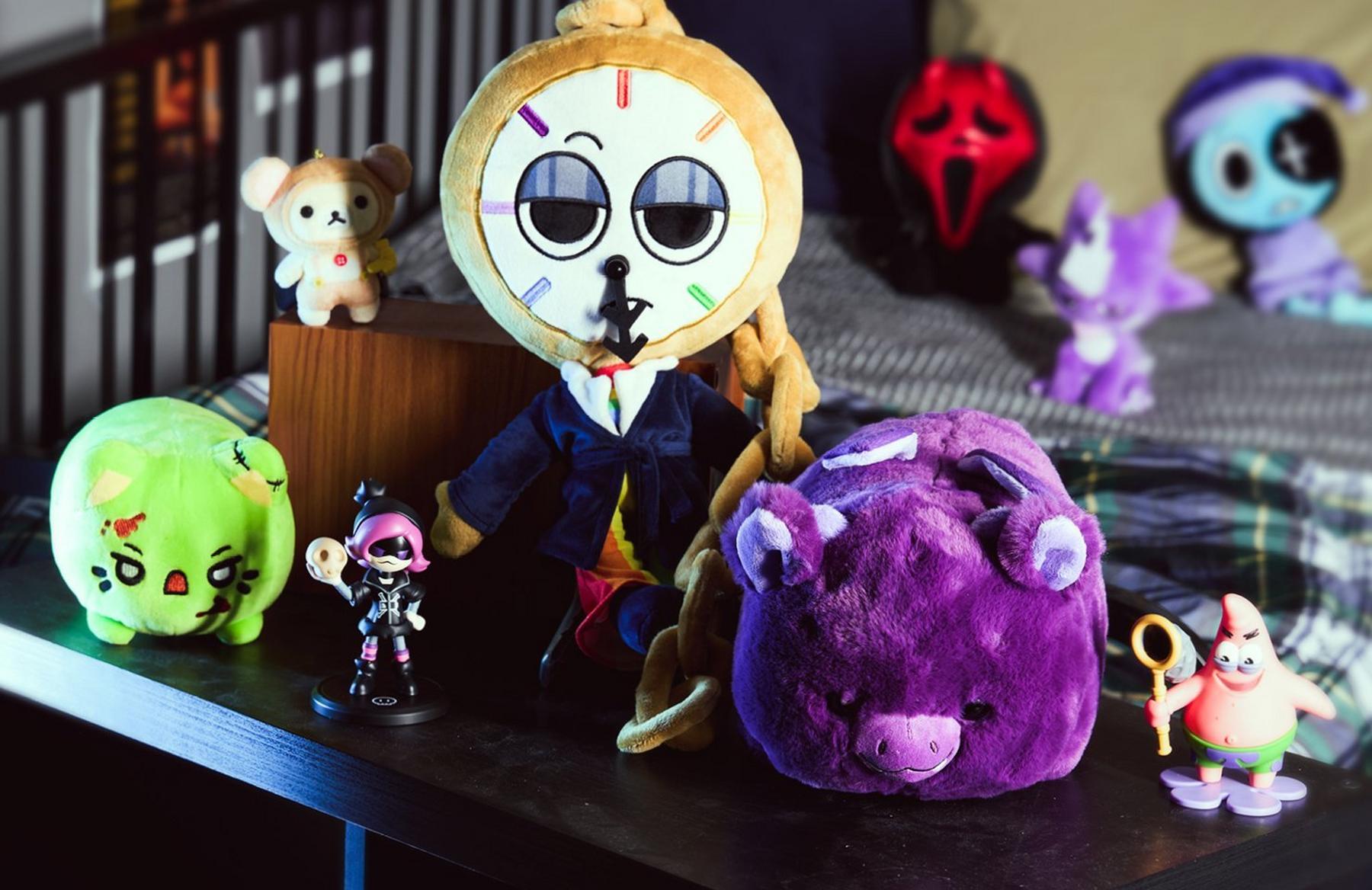 Assorted plush toys and figurines on a table, including a clock-faced doll and purple plush. Shop Now.