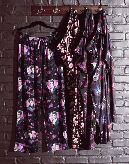 Three pairs of black printed pajama pants hanging on hooks. Shop Now.
