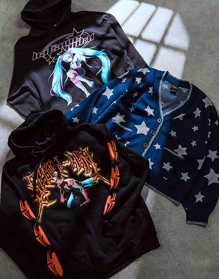 Two black graphic hoodies and a blue star-pattern cardigan laid flat. Shop Now.