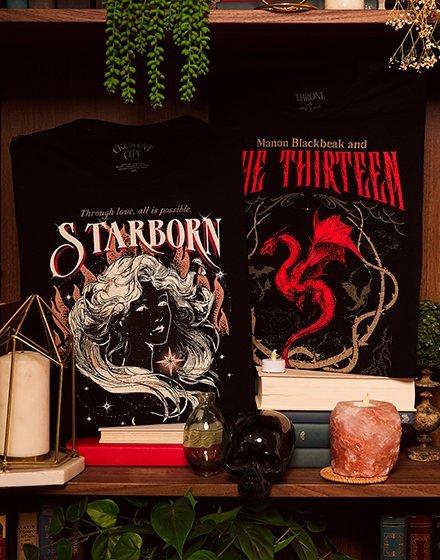 Two fantasy book tees on a shelf, titled “Starborn” and “The Thirteen,” with candles and decor. Shop Now.