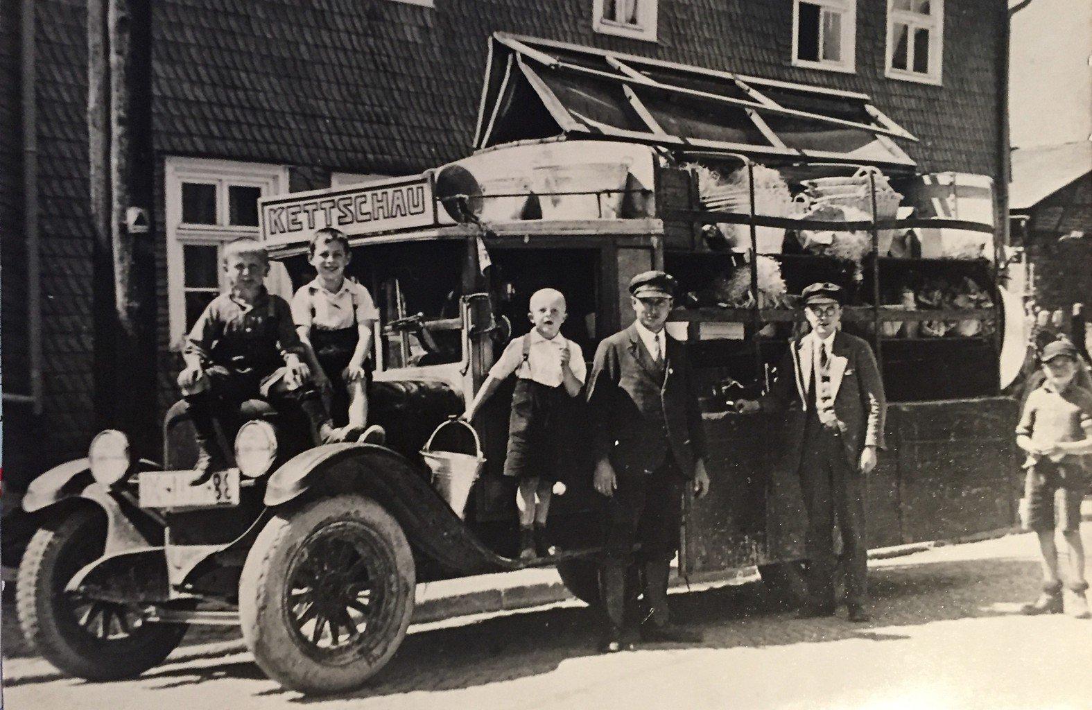 Ein schwarz-weiß Foto von 1925: Ein Wagengeschäft mit der Aufschrift "Kettschau" steht geparkt vor einem Gebäude, 6 Menschen stehen vor dem Wagen und schauen in die Kamera.