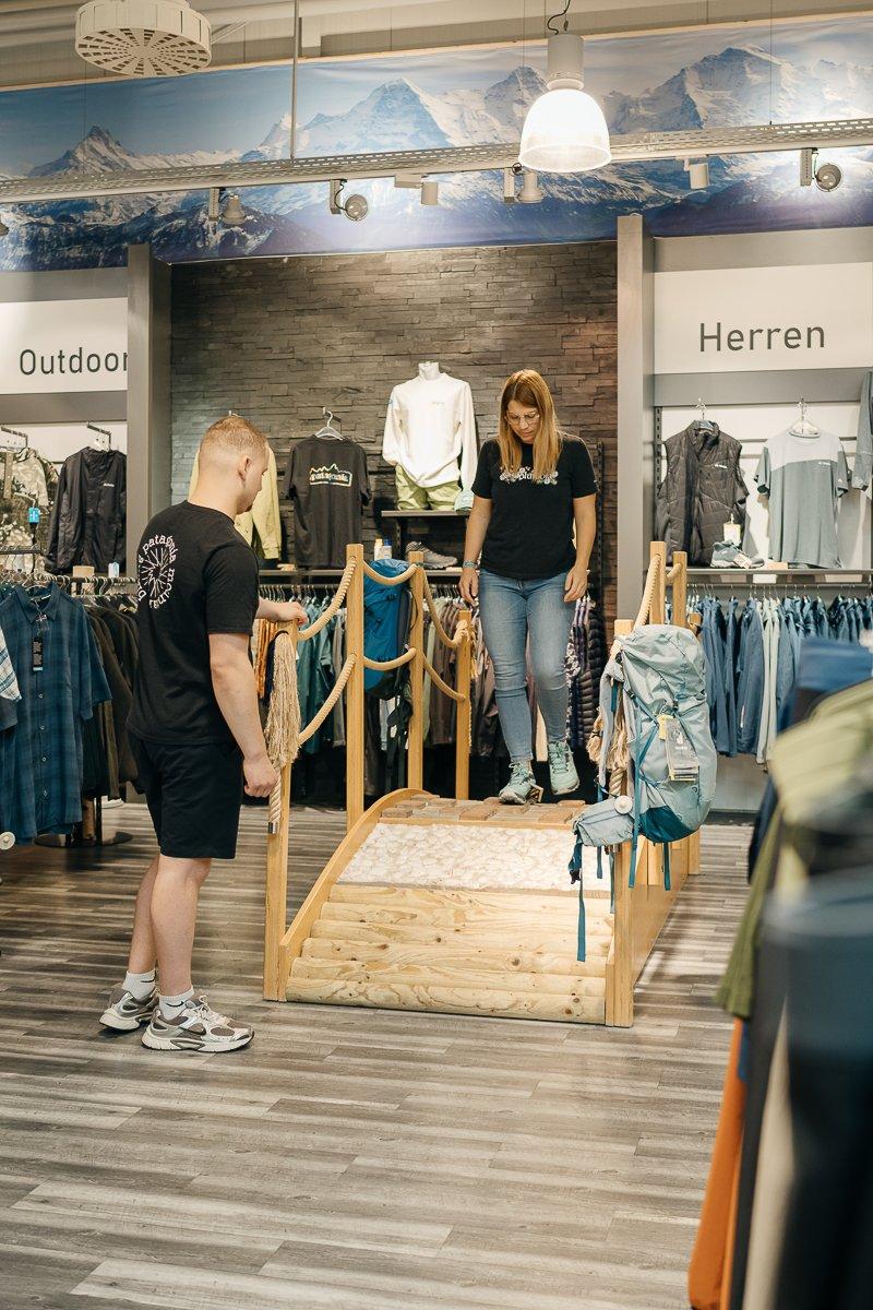 Zwei Menschen stehen vor einem Regal mit Laufschuhen in einem Sportgeschäft und schauen sich die Schuhe an.