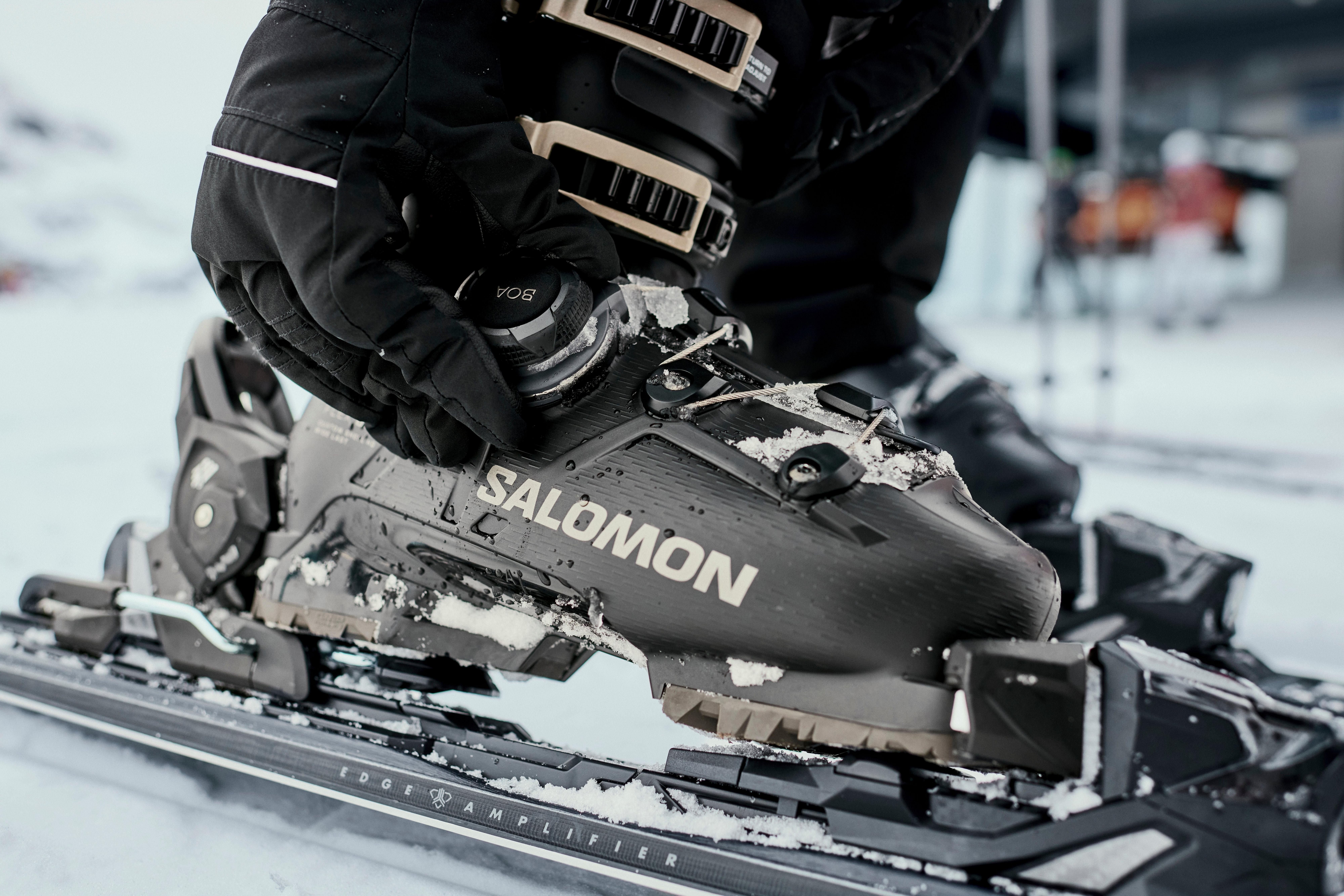 Jemand stellt seine Skistiefel ein, die Person hat die Skistiefel angezogen und steht auf Skiern, Hände in Handschuhen