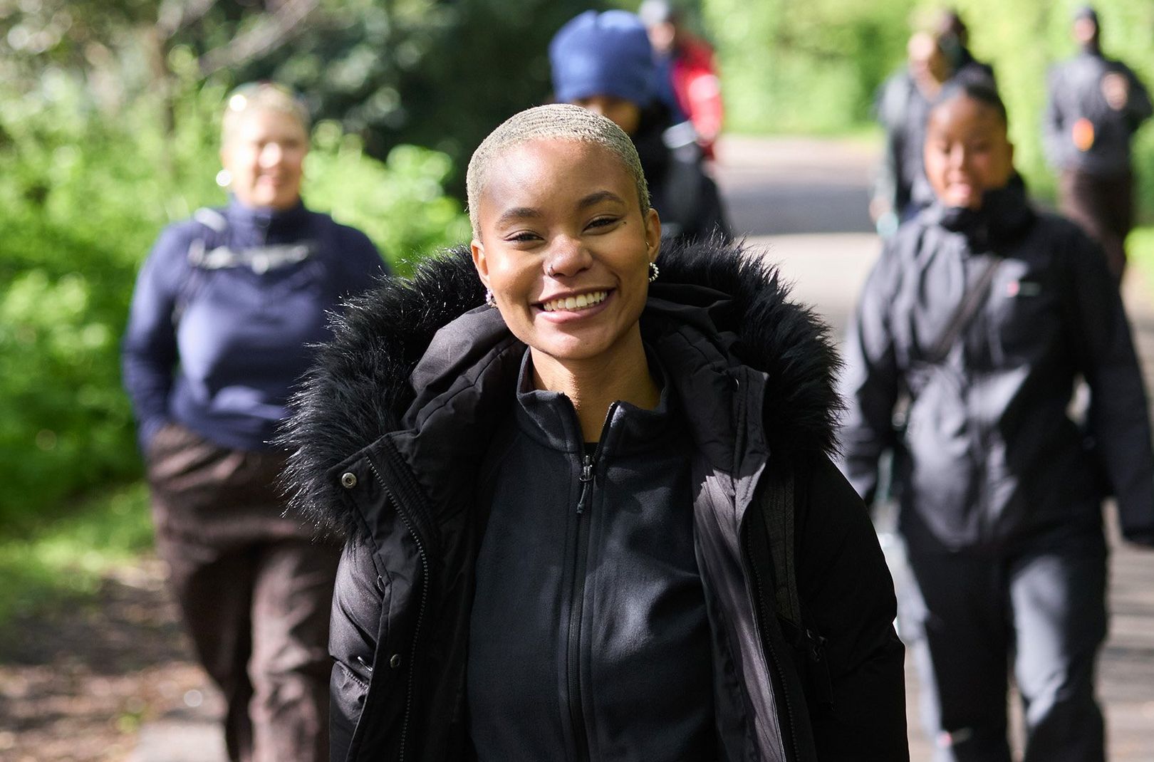 Indira, a Flock Together walk leader, smiling at the camera with members behind