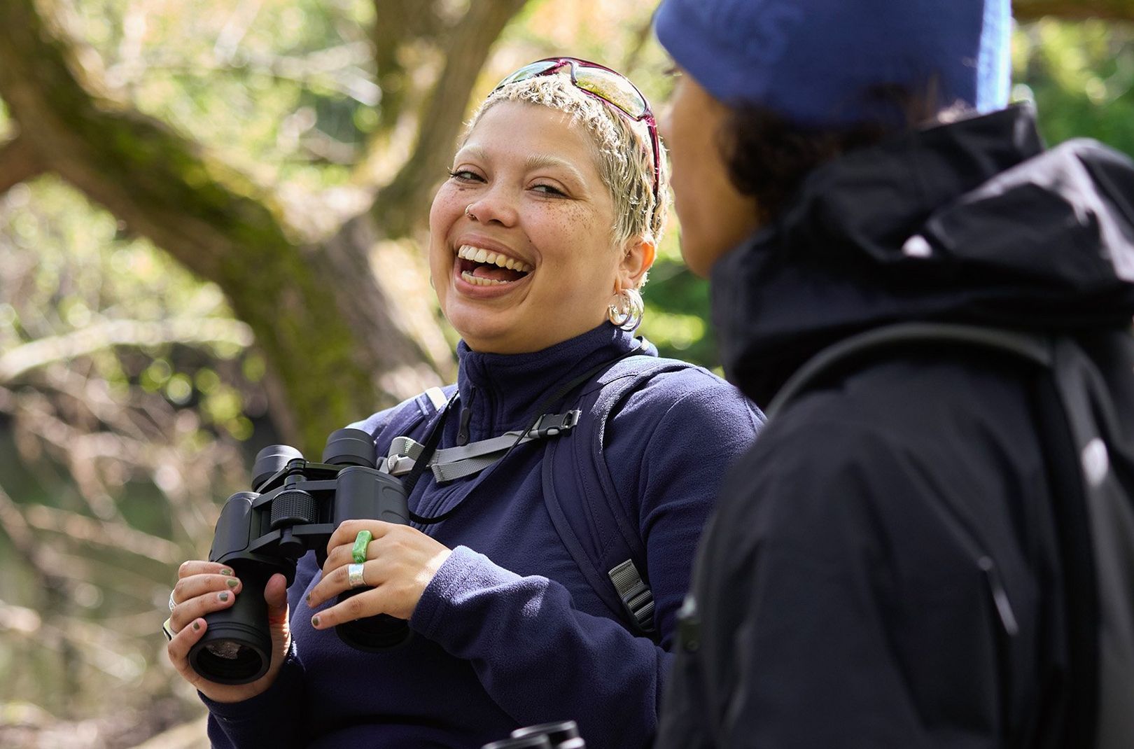 Holly, a Flock Together member, holding some binoculars and laughing with Dennis