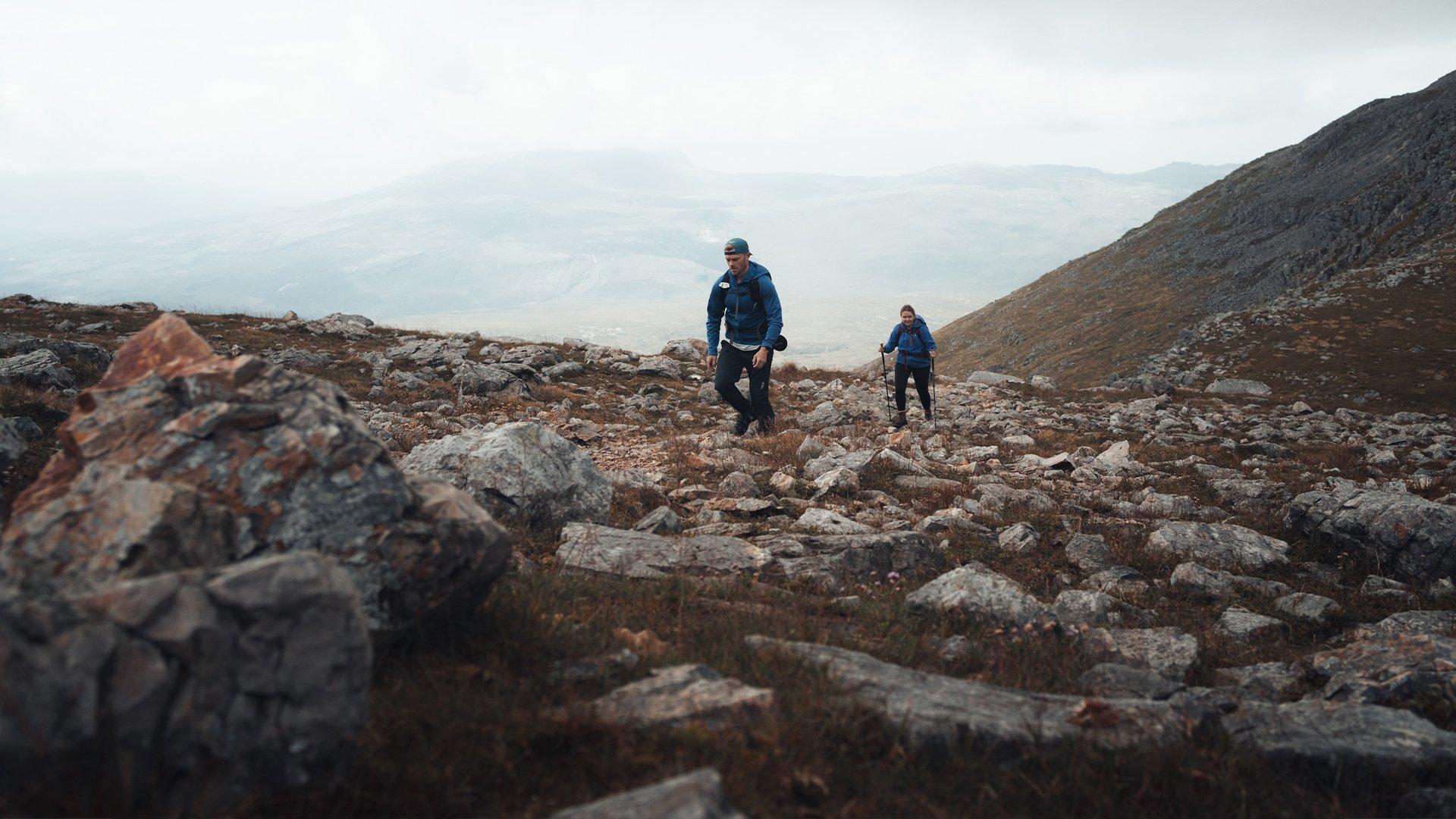 A couple hiking up a rocky mountain path in Scotland