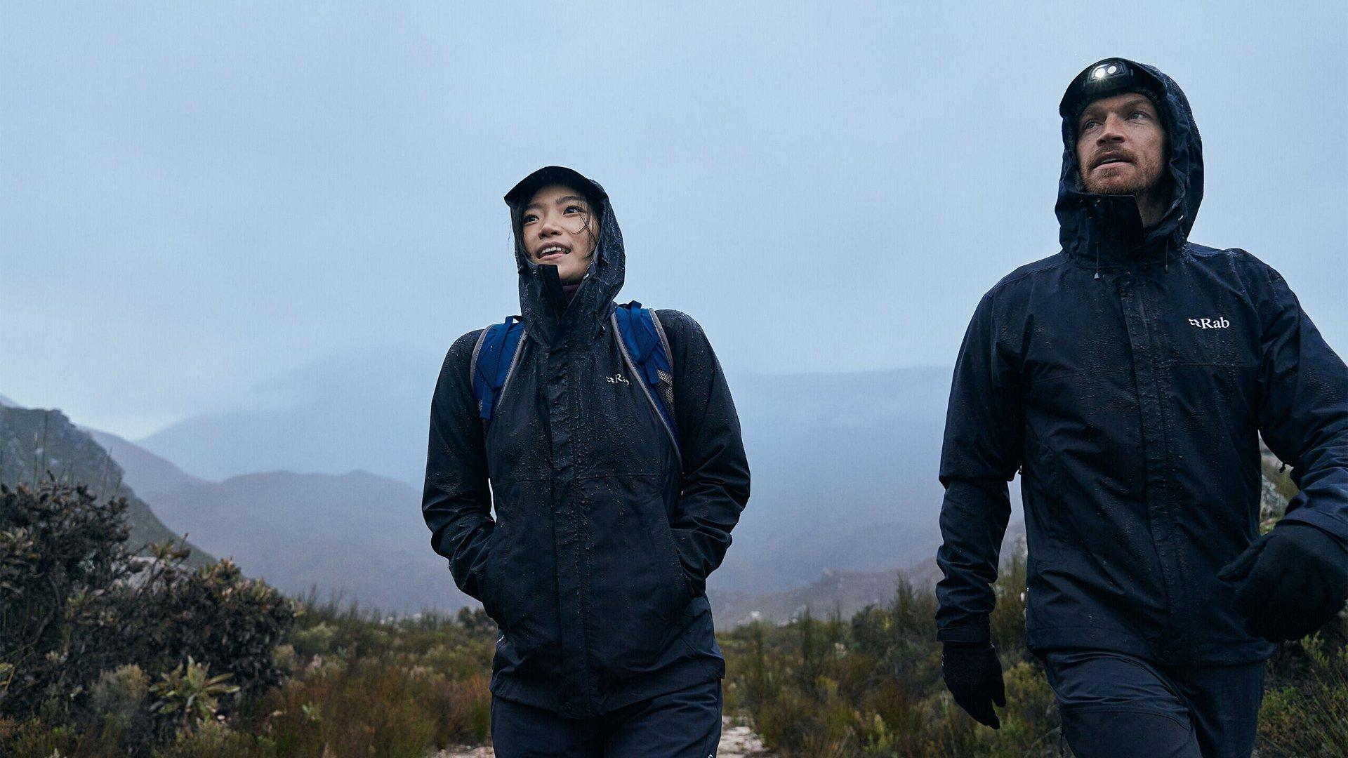 A male and female hiking on a mountain trail together in the rain