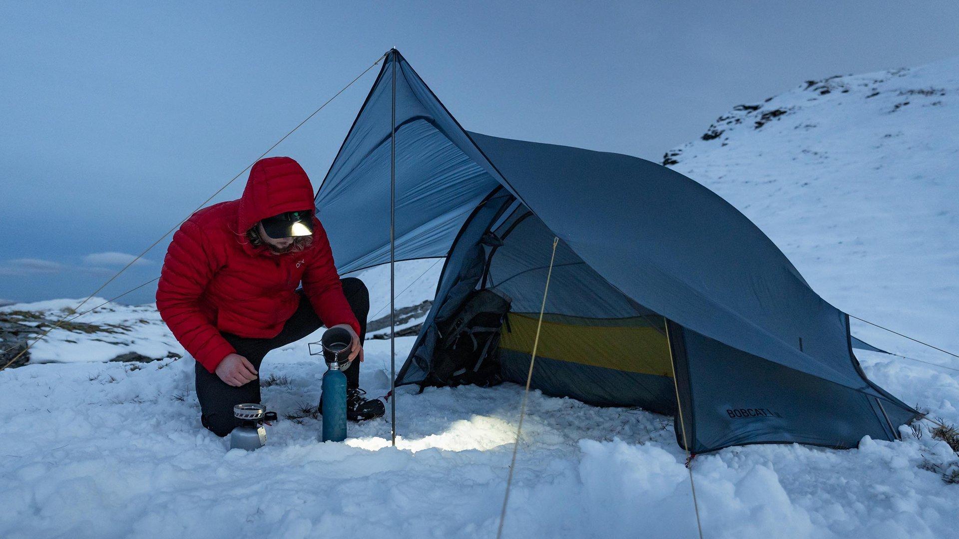 A wild camper making a hot drink at night using a head torch to see