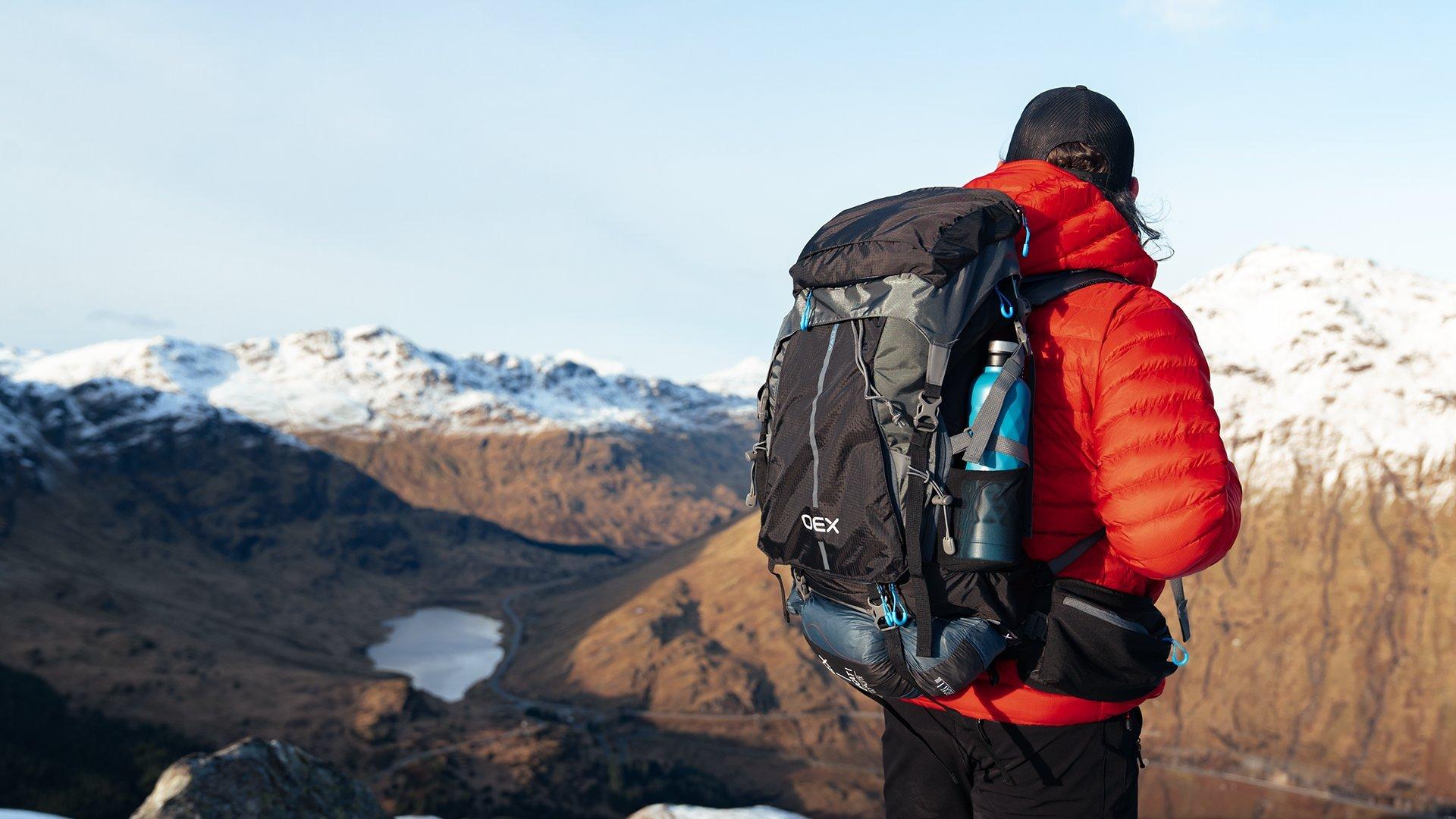 A backpacker looking into a Scottish Glenn during winter from an elevated peak on a snowy mountain hike