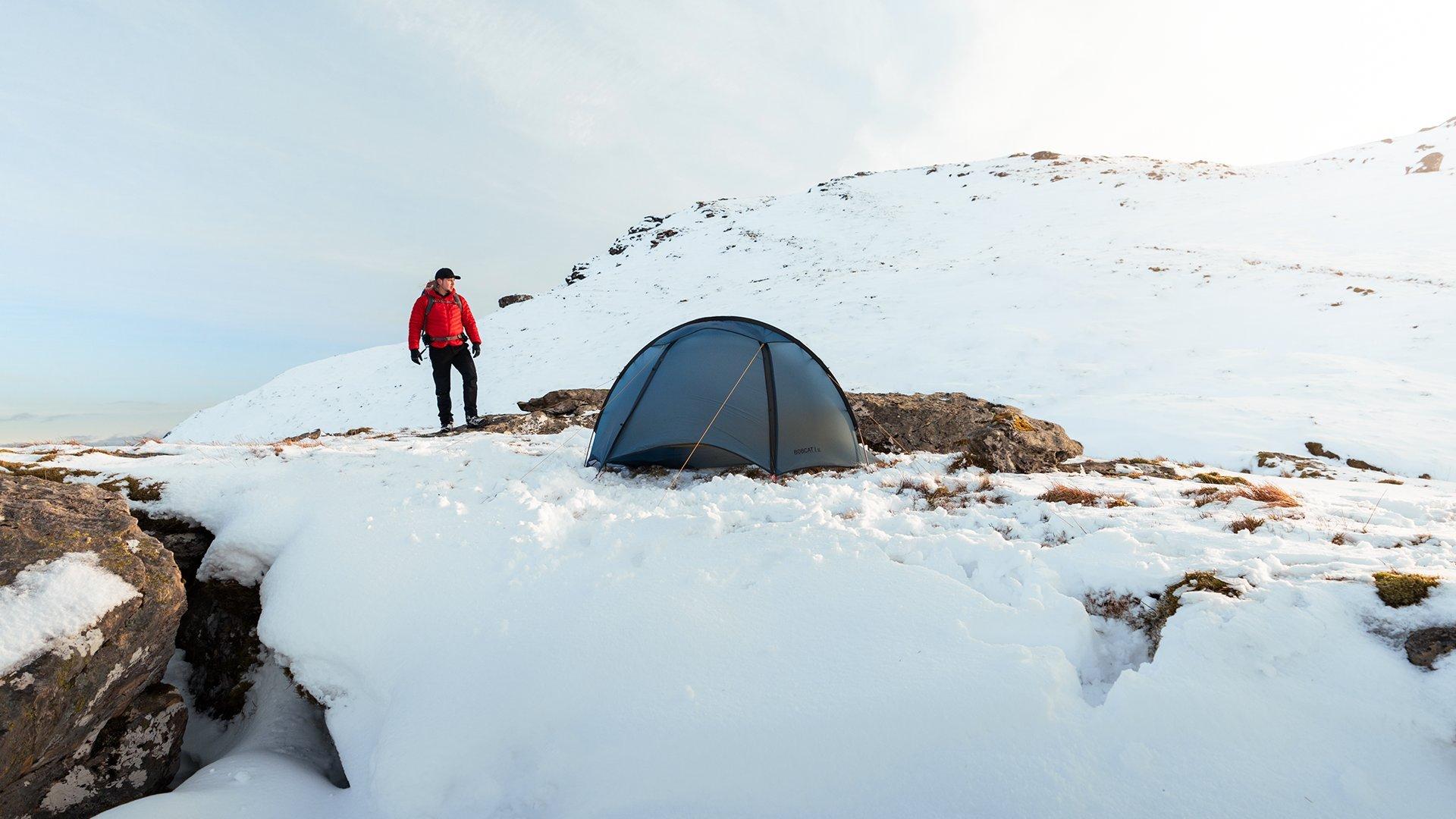 A wild camper approaching a small tent on a snowy mountain in Scotland