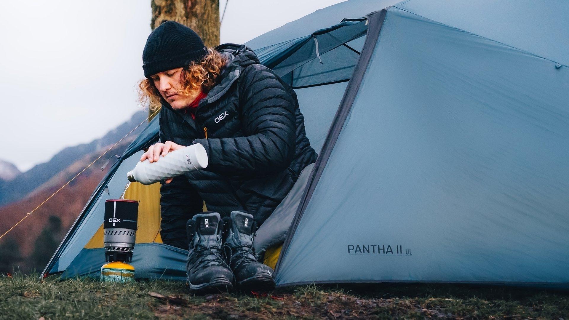 A wild camper making a hot drink while leaning out of their tent during a winter camp